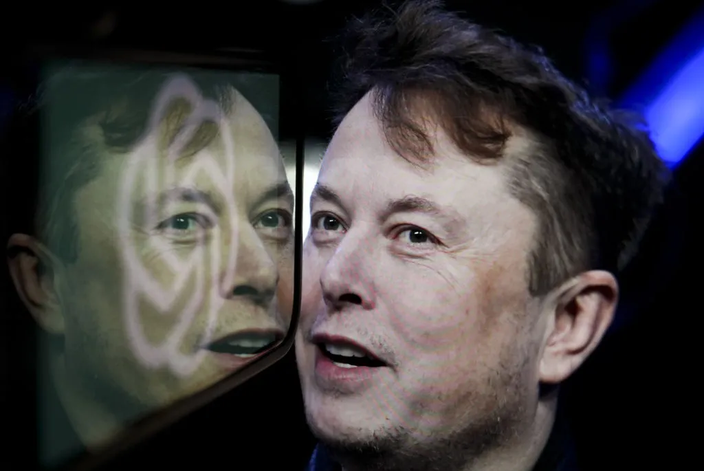 In this photo illustration, the logo of 'OpenAI' is displayed on a mobile phone screen in front of a computer screen displaying the photograph of Elon Musk.
